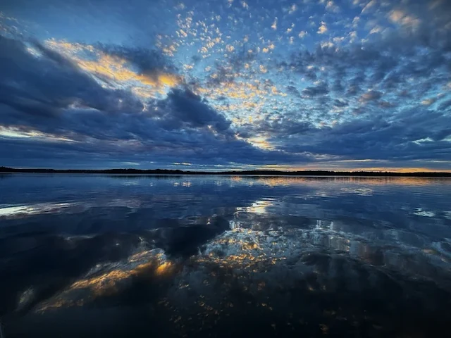 Sunrise over Lake Joseph from Sterling Point, gold-lit cloud mirrored on glass-flat water