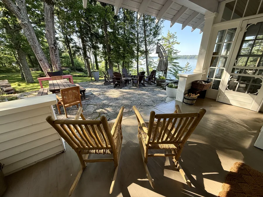 Two wooden rocking chairs on the covered porch at Sterling Point, looking out over the stone patio to Lake Joseph